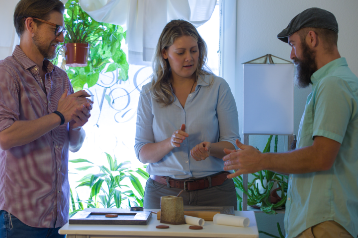 Three people standing around a table with architectural models and plants in the background.