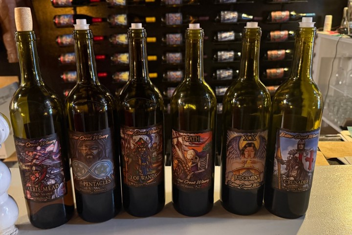 Seven wine bottles with colorful labels stand in a row on a counter.
