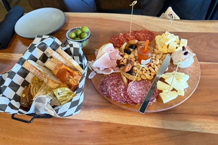 Charcuterie board with meats, cheeses, nuts, bread, olives, and spreads on a wooden table.
