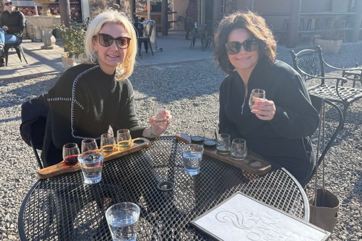 Two women seated at an outdoor table enjoying a flight of drinks under sunny skies.