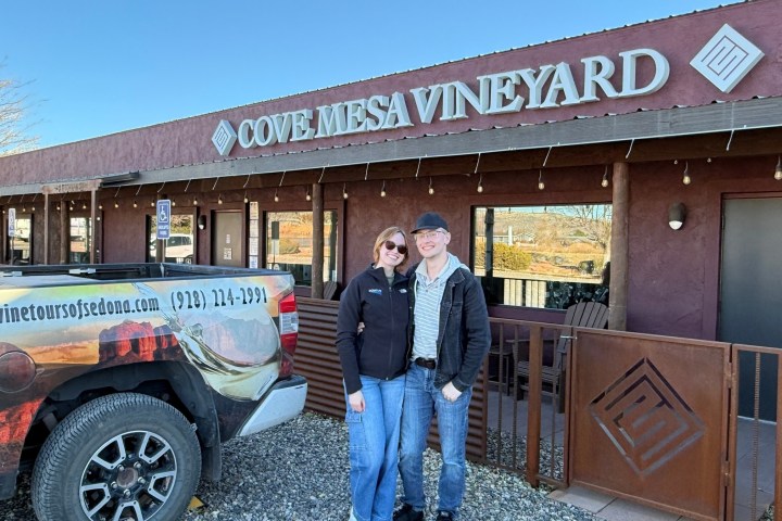 Two people smiling in front of Cove Mesa Vineyard building with a branded truck nearby.
