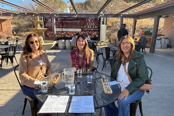 Three women sitting at a table outdoors at a winery with drinks and menus.