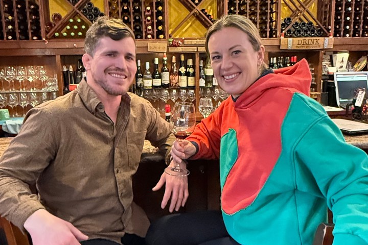 Two people sitting at a wine bar, smiling, with wine racks in the background.