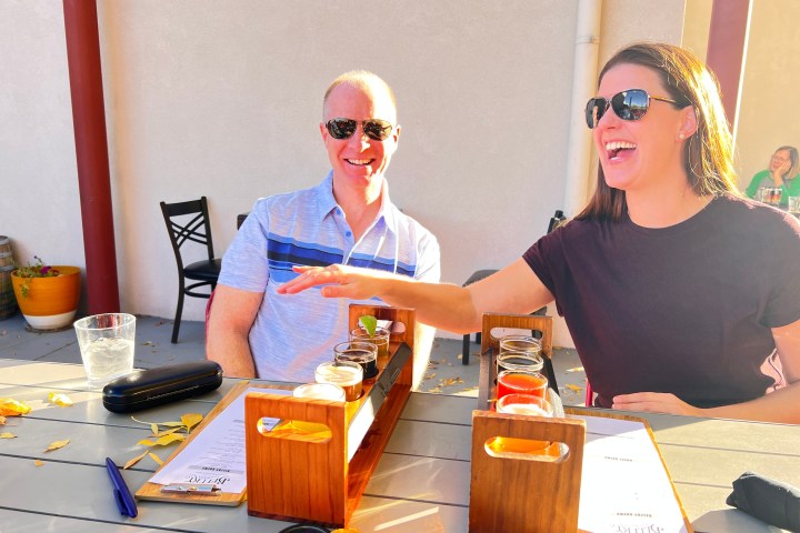 Two people with sunglasses enjoy drinks outdoors, with autumn leaves on the table.