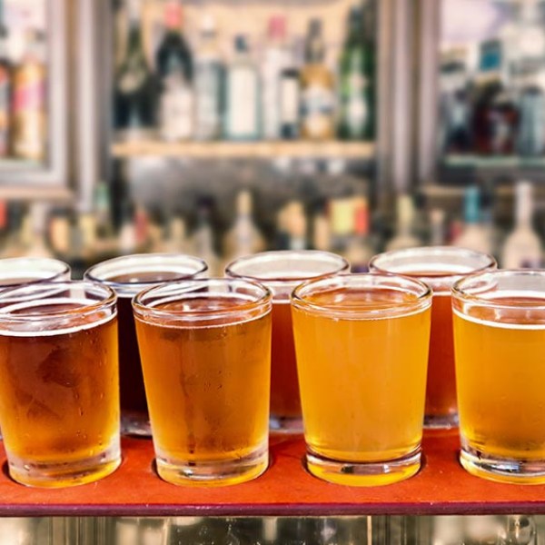 A row of eight beer glasses on a bar counter in a dimly lit setting.