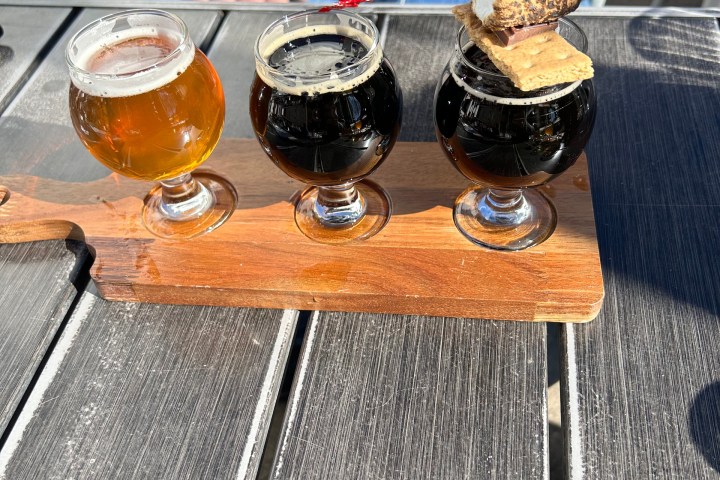 Three glasses of beer on a wooden tray, one with a toasted marshmallow.