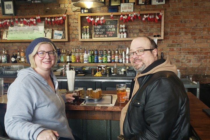 Two people sitting at a bar with drinks, surrounded by festive decorations and bottles on shelves.