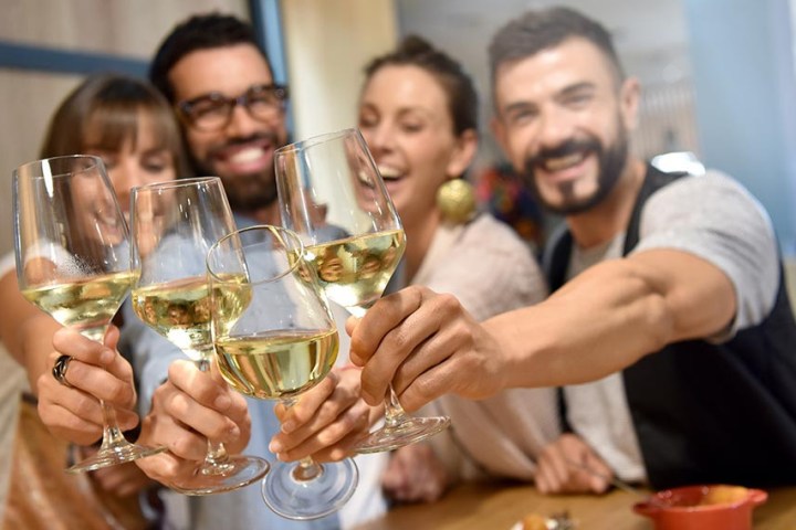 Four people happily toasting with glasses of white wine.