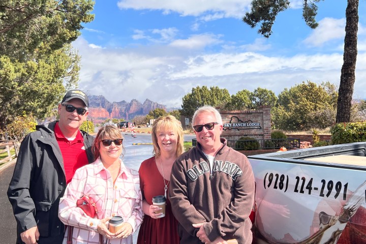 Four people smiling in front of a lodge sign with mountains in the background.