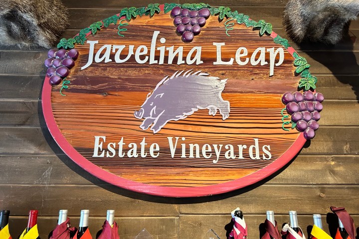 Wooden sign for Javelina Leap Estate Vineyards decorated with grapes above wine bottles.