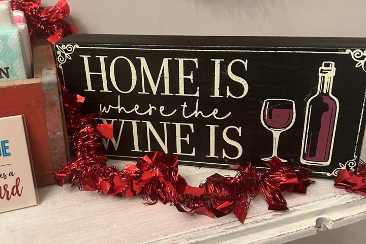 Sign reading 'Home is where the wine is' with a wine bottle image and red garland decor.