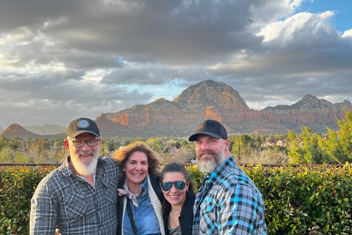 Group of four people smiling in front of a mountain landscape under a cloudy sky.