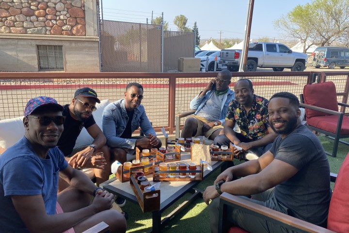 Six men sitting outdoors at a table with drinks and tasting trays.
