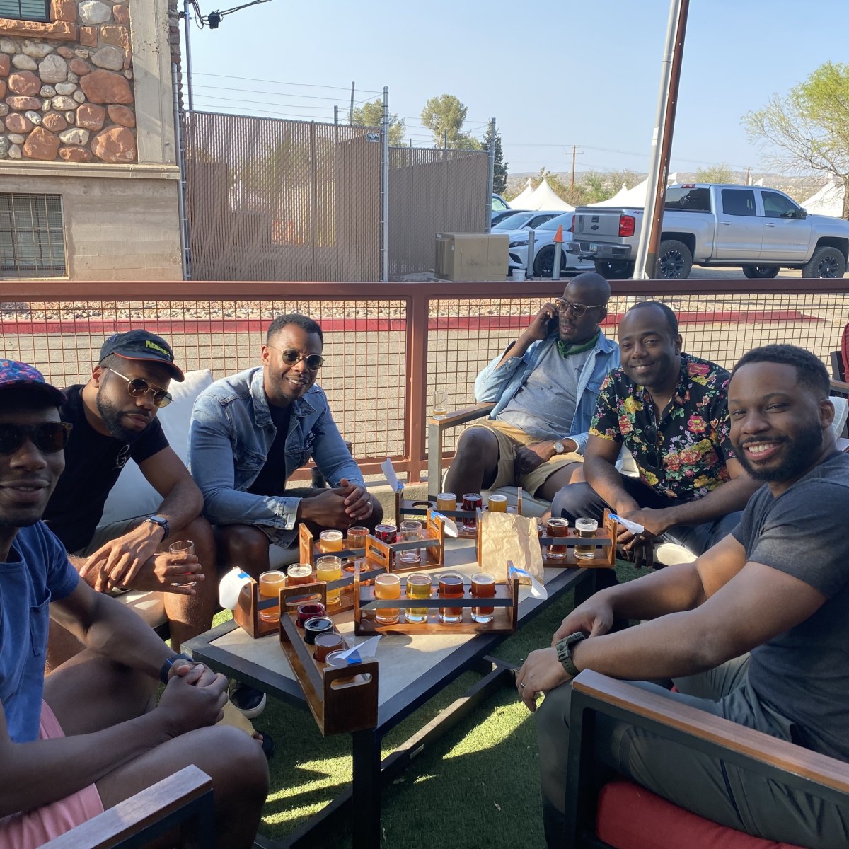 Six men sitting outdoors at a table with drinks and tasting trays.