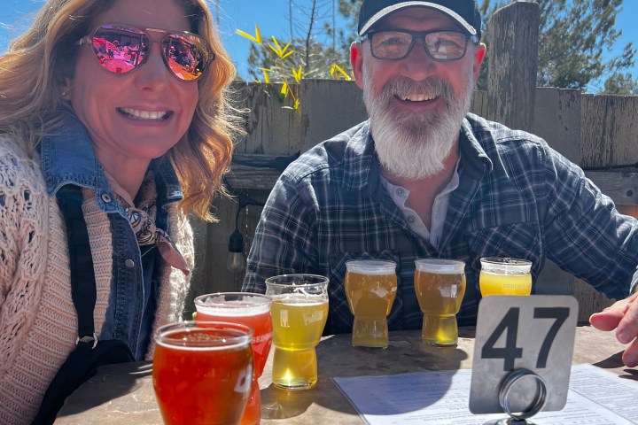 Two people smiling at an outdoor table with glasses of beer and table number 47.