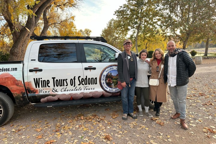 Four people standing beside a 'Wine Tours of Sedona' truck in a park with autumn leaves.