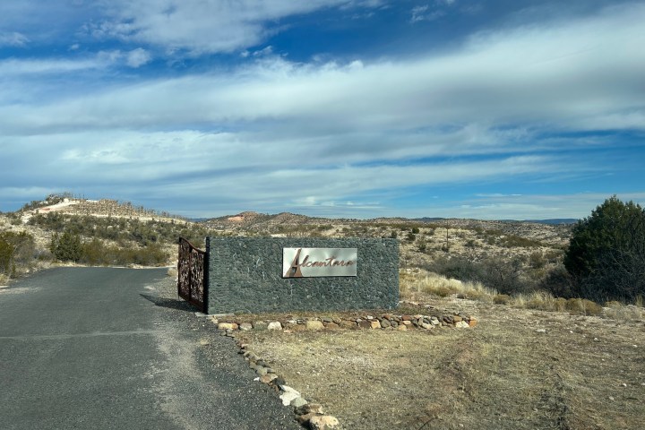 Stone sign with cursive text in a desert landscape under a blue sky with clouds.