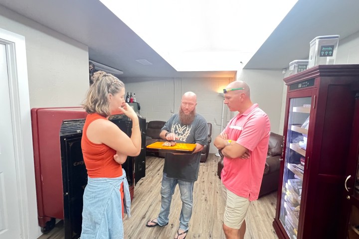 Three people stand in a room, one holding a tray, engaged in conversation.