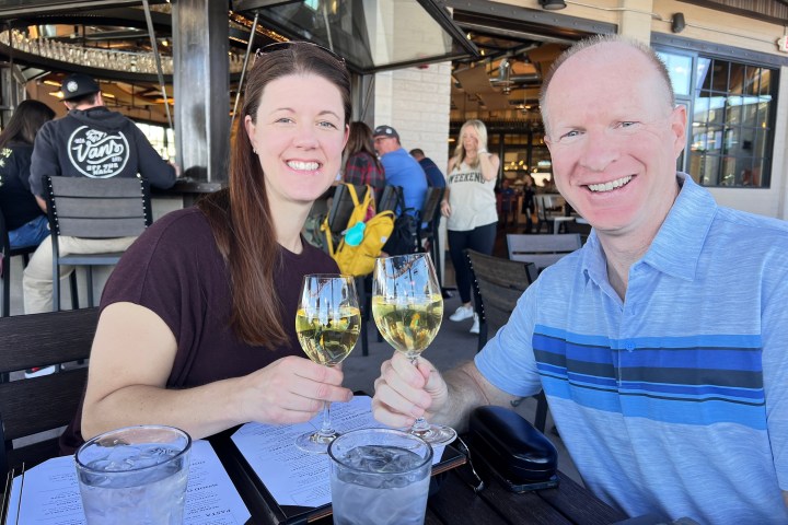 A smiling couple toasting with white wine at an outdoor restaurant table.