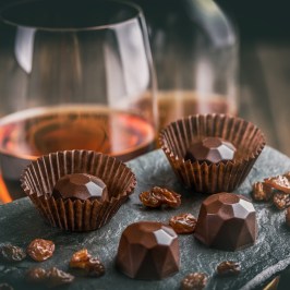 Geometric chocolate pieces and raisins on slate with a glass of amber liquid.