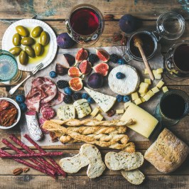 Charcuterie board with cheese, figs, olives, bread, and glasses of red wine on a rustic wooden table.