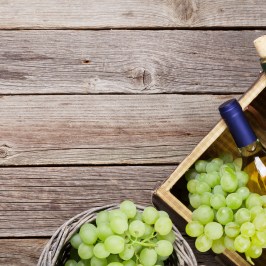 Wine bottles and grapes in a wooden basket on a rustic table.