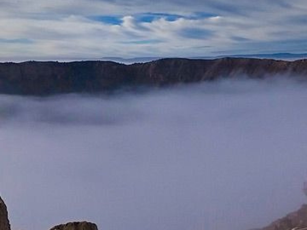Foggy canyon landscape with rocky foreground and cloudy sky.
