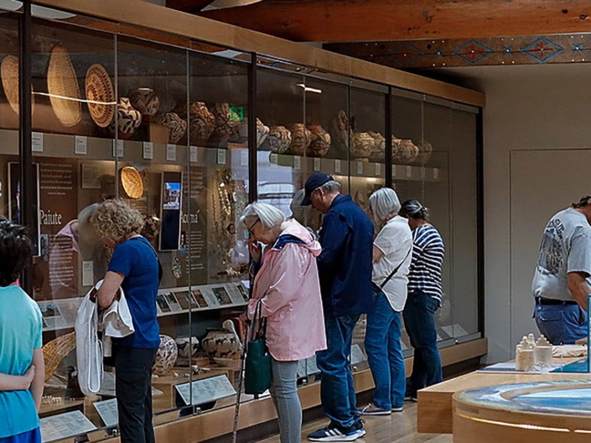 People observe artifacts in a museum exhibit showcasing baskets and pottery.