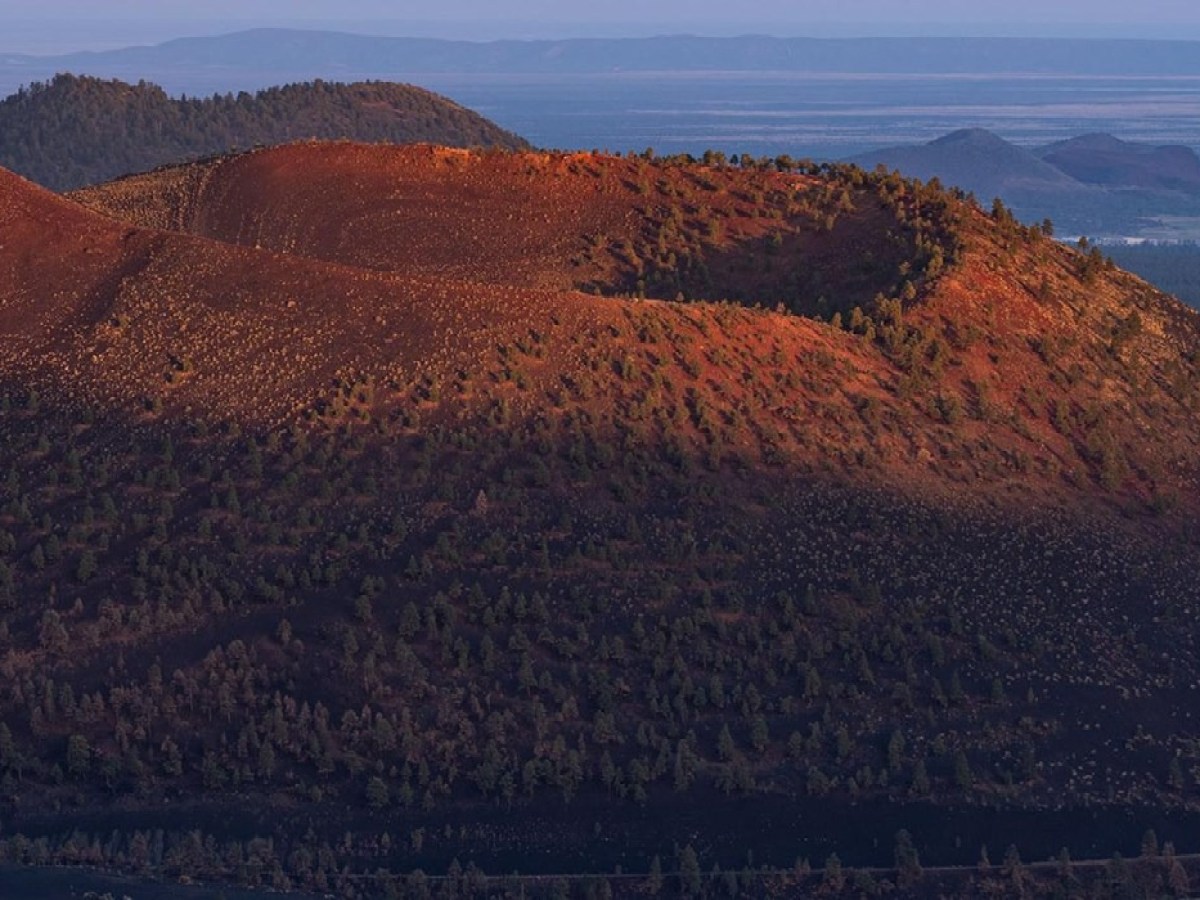 Distant view of a volcanic crater with green vegetation and reddish earth at sunrise.