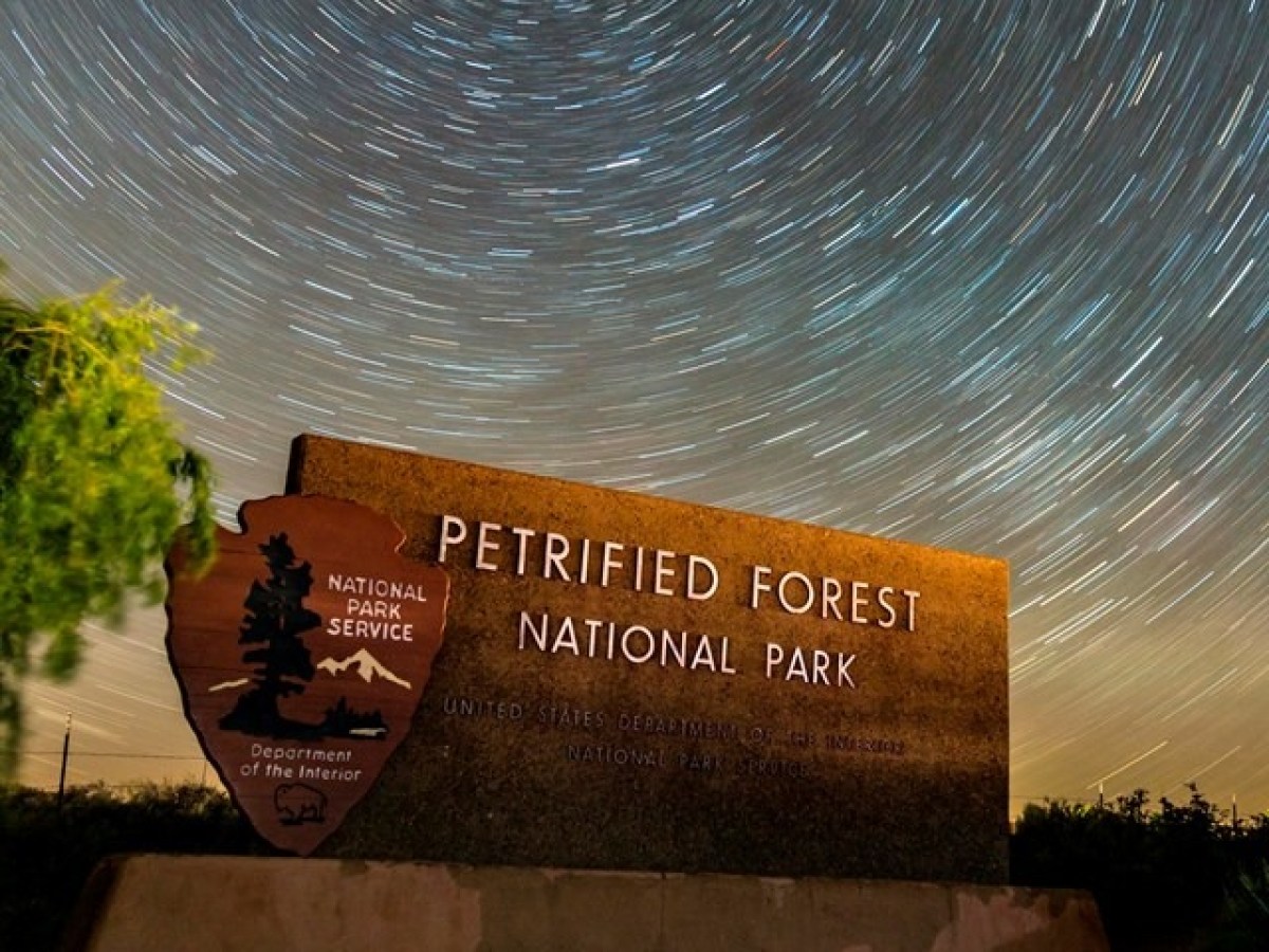 Sign for Petrified Forest National Park under a sky with star trails at night.