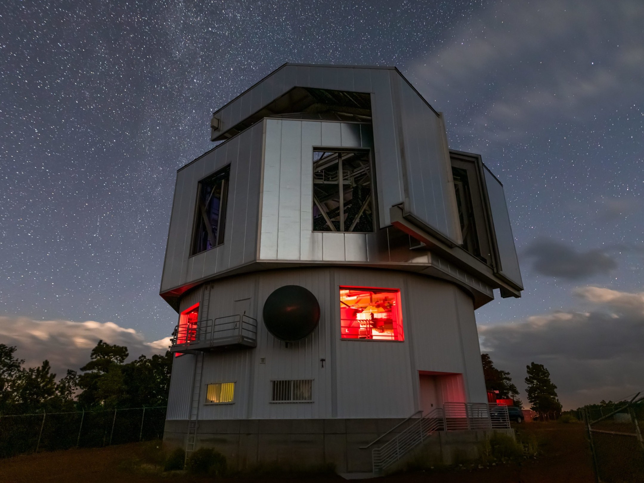 Large telescope building under a starry night sky with glowing red windows.