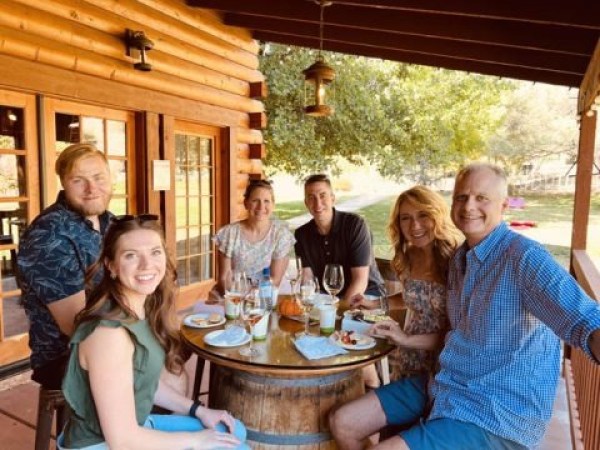 Six people sitting around a table on a wooden porch, enjoying drinks and conversation.