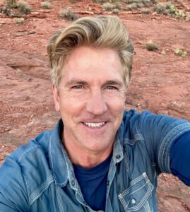 Man in blue shirt smiling in selfie with red rocky background.