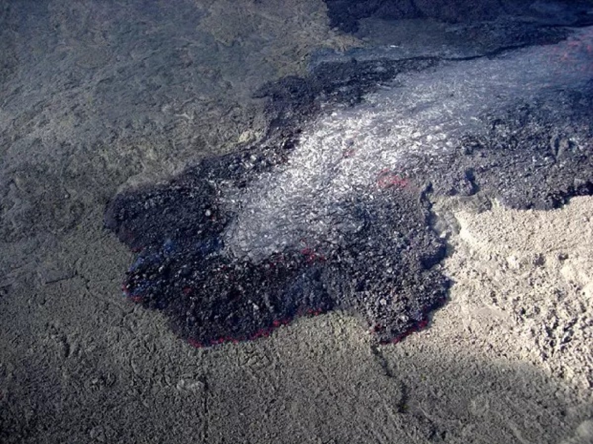 A cooled lava flow with a crusty, cracked surface and dark, uneven texture on volcanic rock.