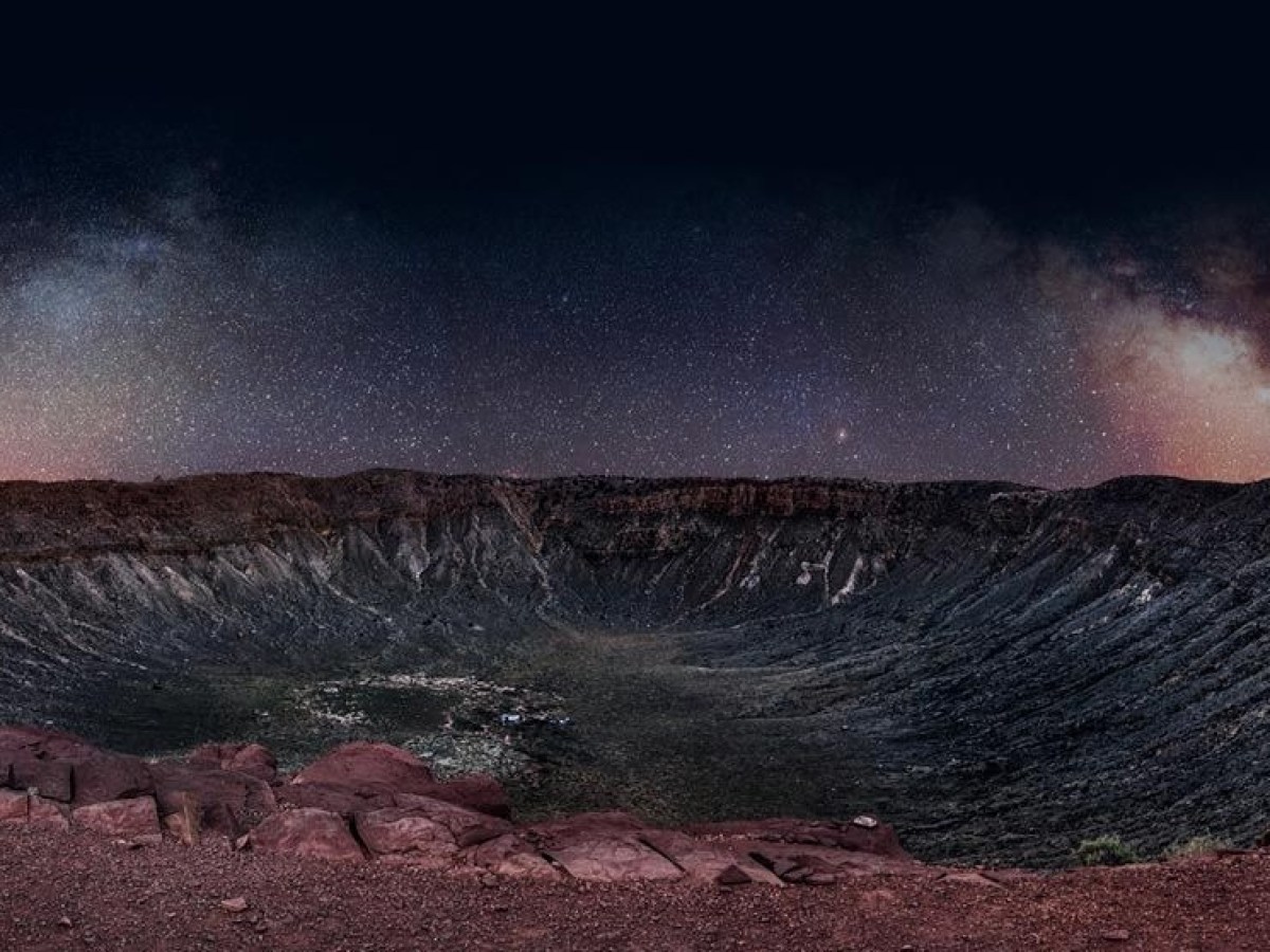 Meteor crater under a starry night sky with red rocky foreground.