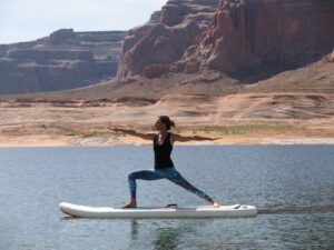 Person doing yoga on a paddleboard in a lake with rocky cliffs in the background.