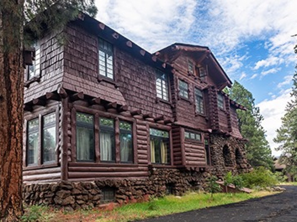 Large wooden cabin with stone foundation and multiple windows under a partly cloudy sky.