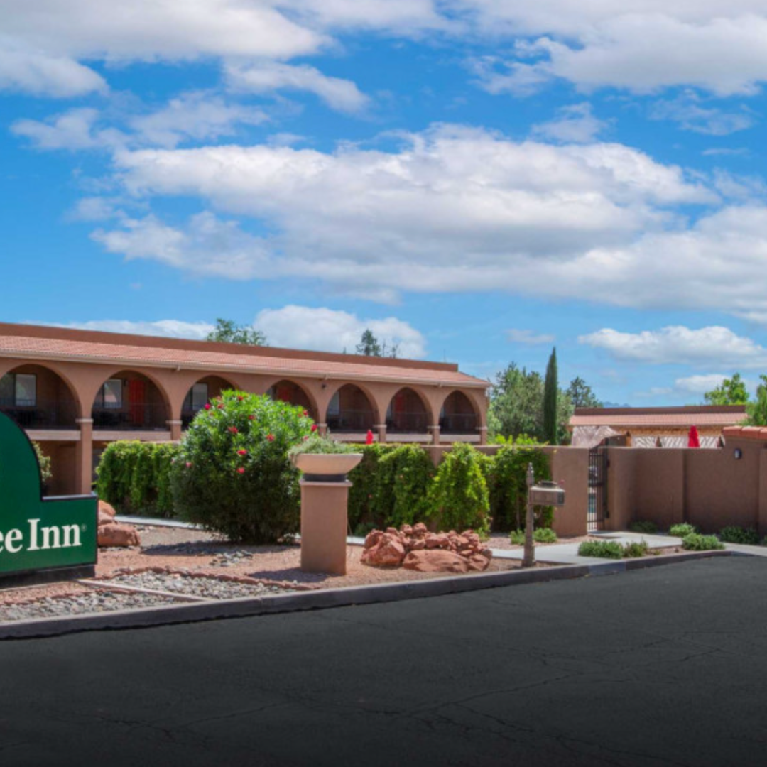 GreenTree Inn with brown building, green trees, and blue sky with clouds.