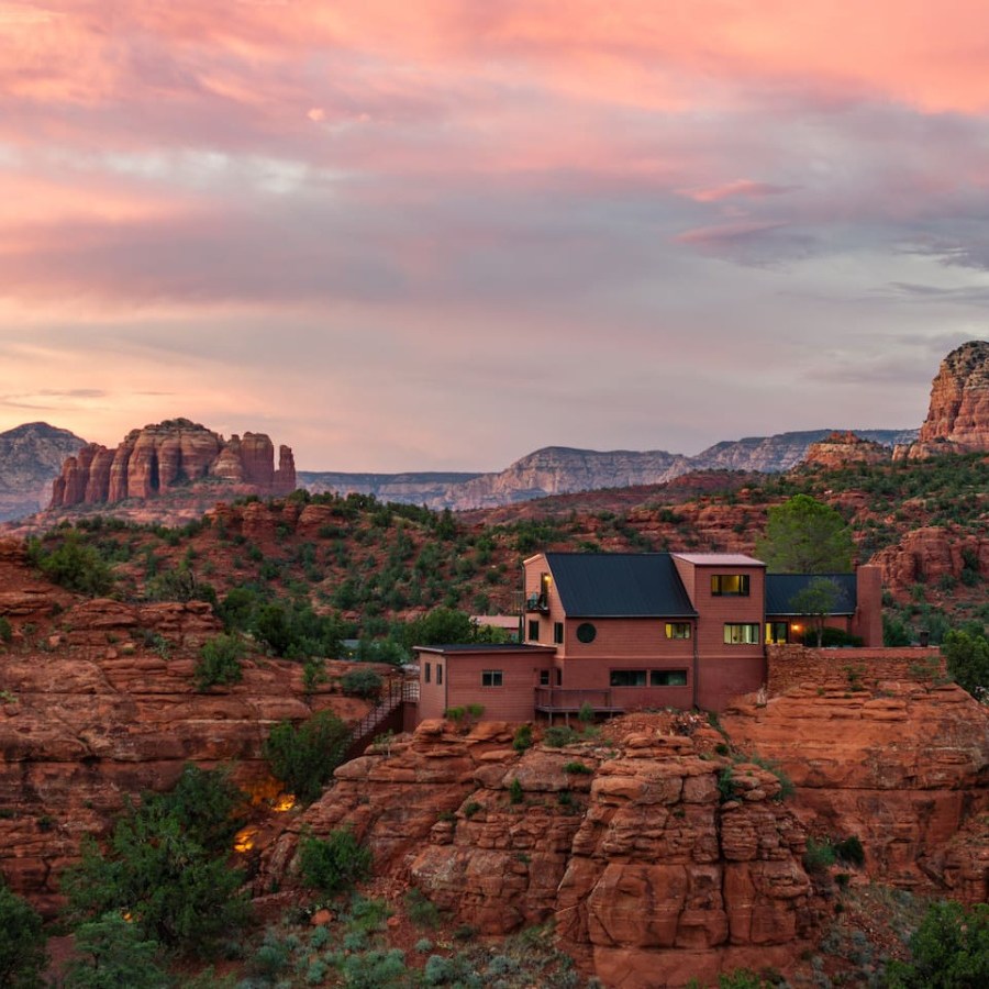 Sunset over a modern house on red rock cliffs with distant mountains.