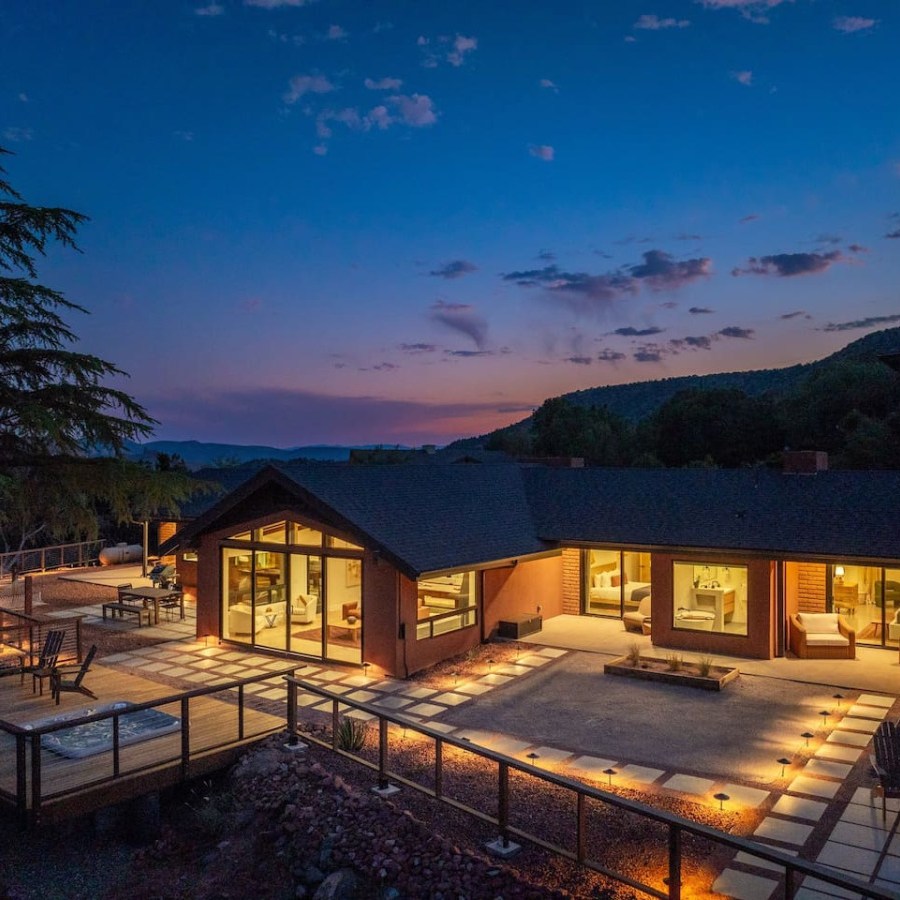 A modern house with large windows at dusk, surrounded by trees and outdoor lighting.