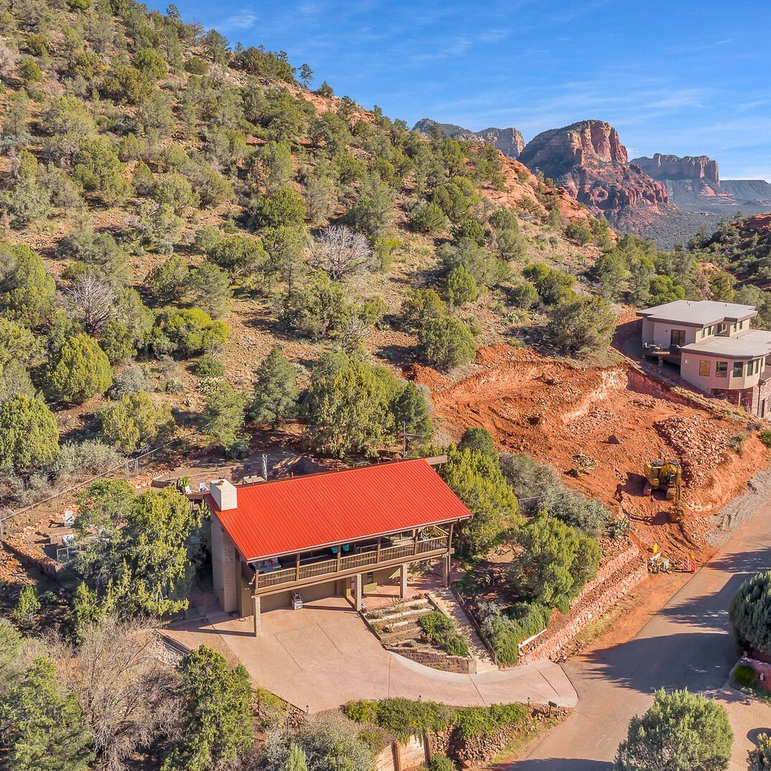 Hillside homes with red roofs in a desert landscape with red rock formations and vegetation.