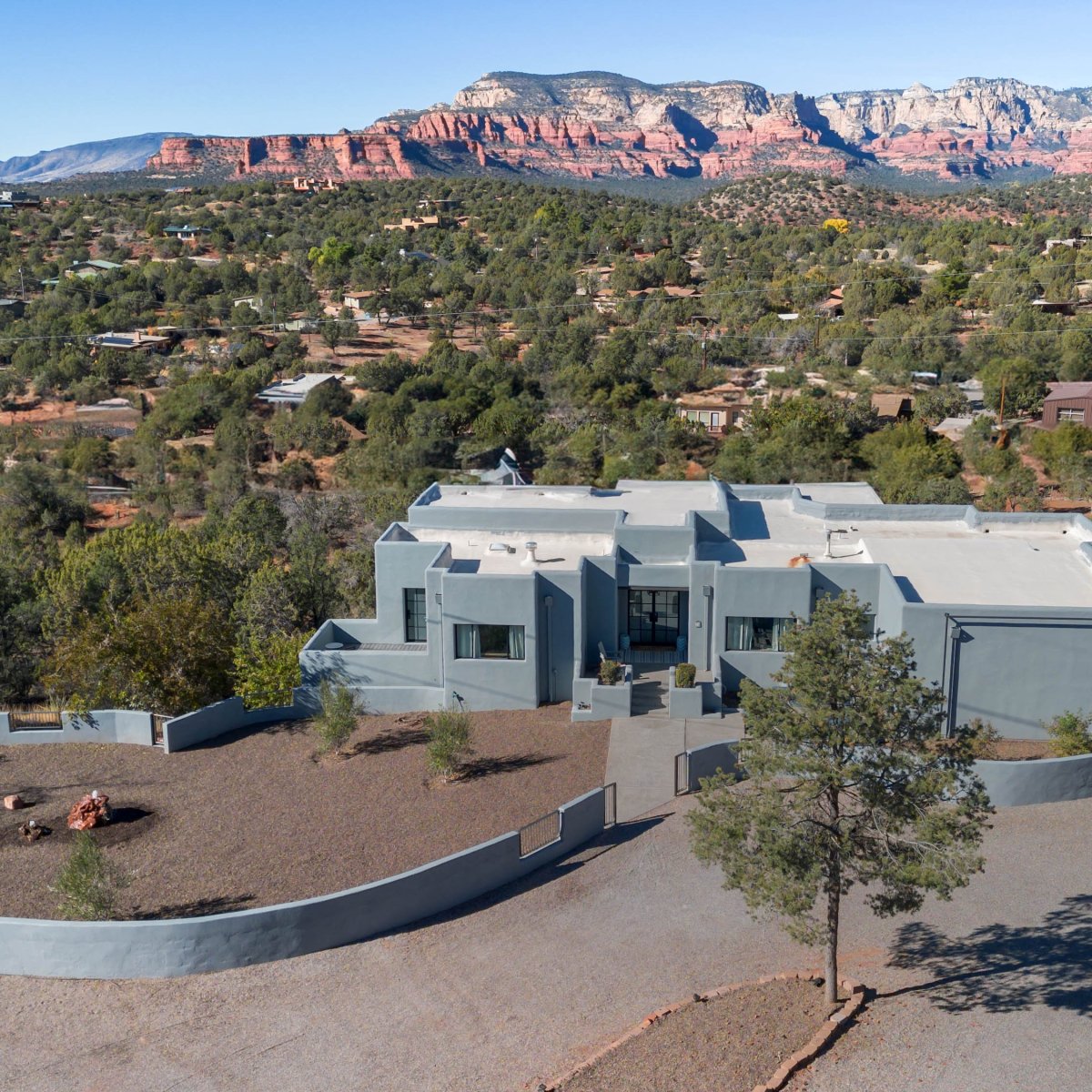 Modern house with flat roof, surrounded by desert terrain and distant red rock formations.