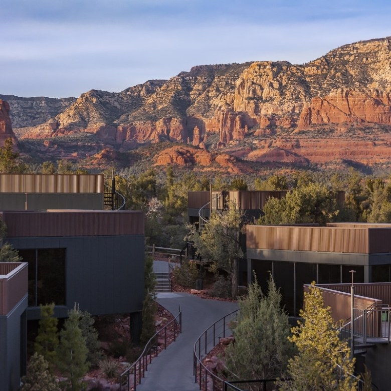 Modern buildings surrounded by trees, with red rock mountains in the background.