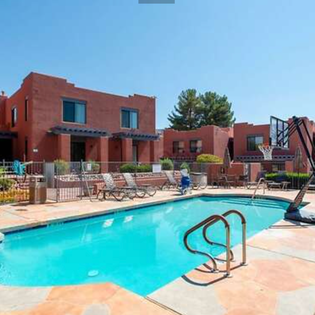 Outdoor pool with chairs and red brick buildings under a clear blue sky.