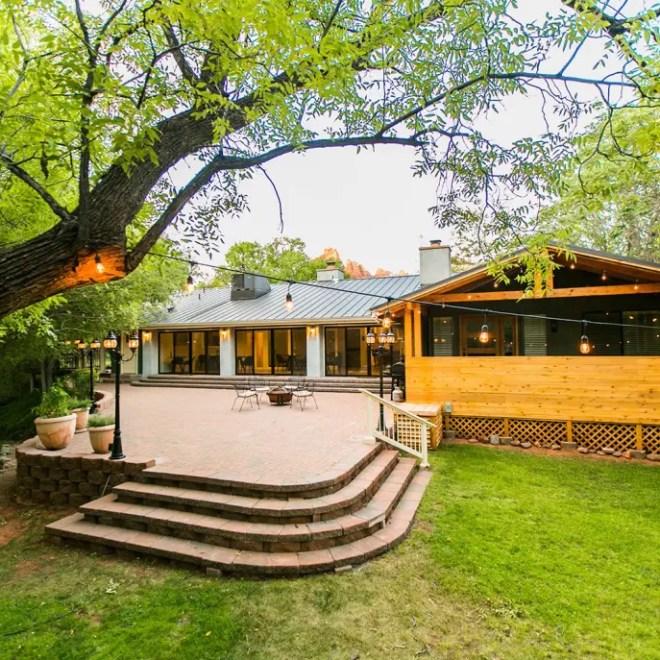 Cozy house with large patio, wooden deck, green lawn, and string lights under a tree.