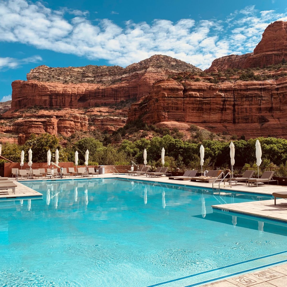 Pool with loungers, umbrellas, and red rock canyon backdrop under blue sky.