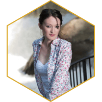 Woman in floral blouse near a railing with rocks in the background, framed in a hexagon.