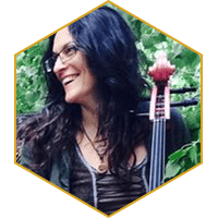 Woman with dark hair and glasses smiling, holding a cello outdoors.