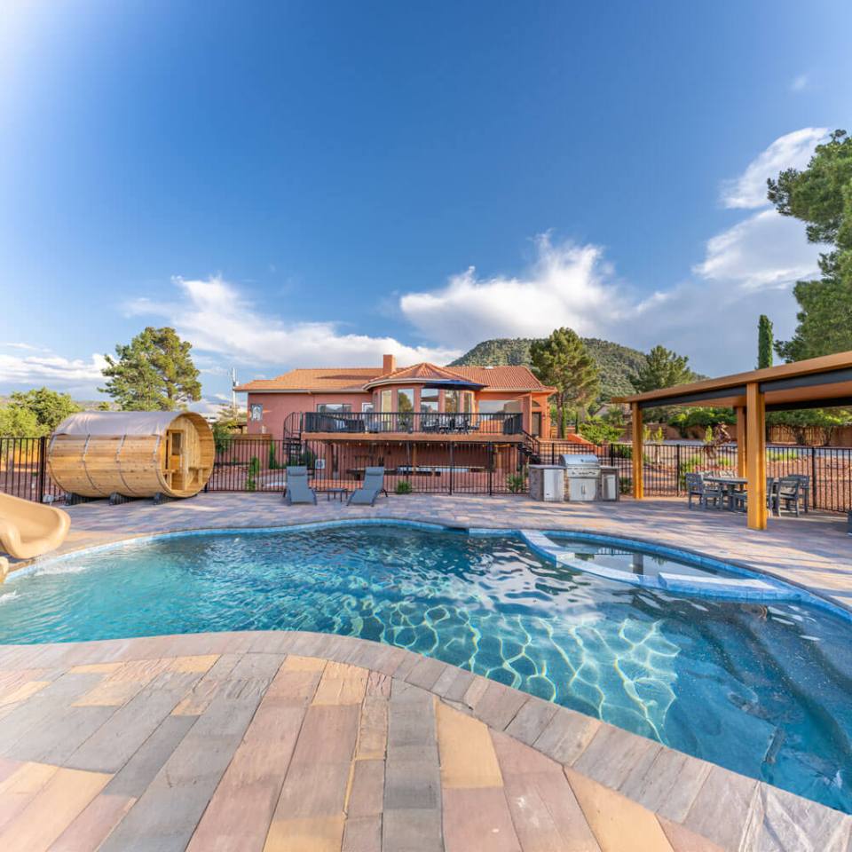 House with pool, lounge chairs, and round sauna under a blue sky with clouds.