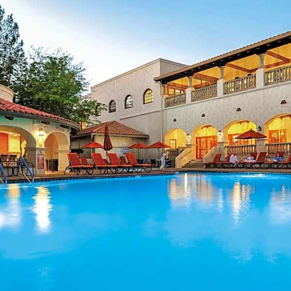 Outdoor pool with lounge chairs, umbrellas, and villa-style building at dusk.